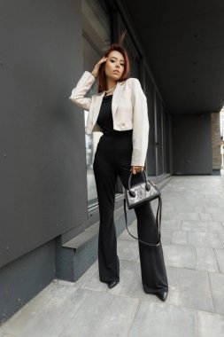 Resmi giyinmiş çekici genç profesyonel şehir ortamında el çantasıyla ayakta duruyor. Modern iş modası. Bir kadının tam boy portresi