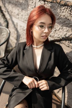 Zarif siyah elbiseli ve benekli taytlı modern bir kadın açık havada güneşli bir günün tadını çıkarıyor. Işıktan yapılmış bir yıldızla süslenmiş bir kafenin duvarında rahatça oturuyor..