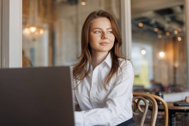 Laptopunu kullanarak şık bir kafede uzaktan çalışan bir işçi. Benekli tayt ve şık bluz gibi şık detaylar bu modern iş ortamına moda yeteneği katıyor..