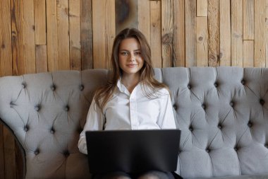 Kendine güvenen bir kadın şık bir kafede otururken dizüstü bilgisayarında çalışıyor. Rahat ve modern uzak ofis ortamı.