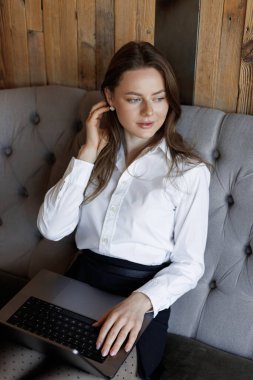 Dizüstü bilgisayarda uzaktan kumandalı bir kadın, ahşap duvarları olan rahat bir kafede rahat bir koltukta oturuyor. Rahat ve üretken çalışma ortamı.