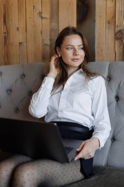 Şık bir kahve dükkanındaki rahat bir kanepede dizüstü bilgisayar kullanarak işine odaklanmış bir kadın profesyonel..