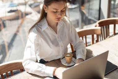 Kahve ve akıllı telefonlu bir kafede dizüstü bilgisayarda çalışan bir iş kadını. Modern serbest yaşam tarzı, uzak çalışma, profesyonel atmosfer
