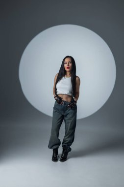 Hareketli kıyafetli ve eldivenli modacı kadın dramatik ışıklandırması olan minimalist bir stüdyoda poz veriyor..