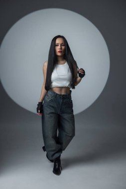 Beyaz bluzlu ve kot pantolonlu Asyalı şık bir bayan model dairesel spot ışıklarının altında güvenle yürüyor. Şehir tarzı, tutumu ve gücü olan moda portresi. Güzel bayan.