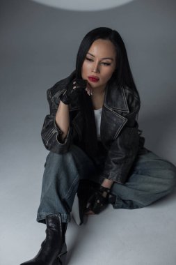 Kendine güvenen bir kadının modern moda portresi sıradan bir kot ve deri içinde. Sanatsal dairesel ışıklandırma altında güçlü duruş ve yoğun bakış.