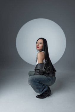 Şık şehir modasını cesur makyaj ve dramatik pozlarla sergileyen şık bir model. Deri, kot ve sahne ışıkları altında kendine güven. Asyalı güzel kadın