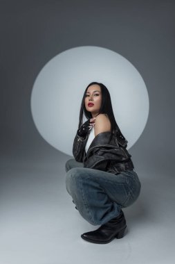 Sıradan sokak kıyafetleri giyen moda bir kadının portresi dramatik ışıklandırmalı bir stüdyoda oturuyor. Moda, tutum ve bireysellik. Asyalı güzel kadın