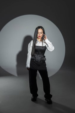 Moda kıyafetli, kendine güvenen genç bir kadın halka ışıkları altında dikiliyor. Cesur ifade ve tarzla minimalist moda konsepti. Asyalı güzel kadın