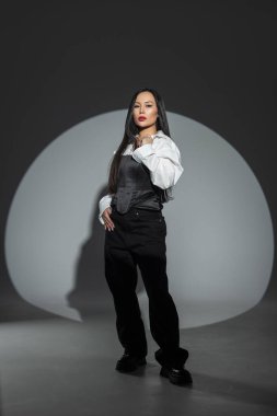 Monokrom kıyafetli şık bir kadın dramatik spot ışıkları altında güven içinde poz veriyor. Moda, tavır ve stüdyo portresindeki modern zarafet..