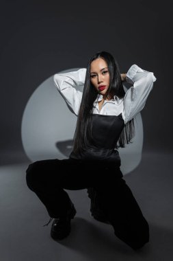 Modayı takip eden kadın model dairesel bir ışığın altında tek renkli kıyafetle yerde oturuyor. Minimalist tarz, karamsar atmosfer. Asyalı güzel kadın.
