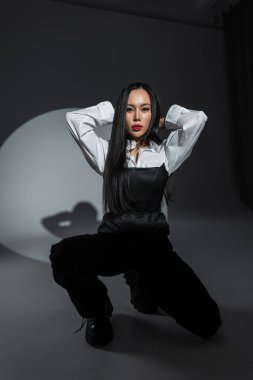 Karanlık stüdyo ortamında, cesur moda giyinen ve dramatik ışıklandırma altında kendine güvenen genç şık bir kadın. Minimalist, kentsel estetik.