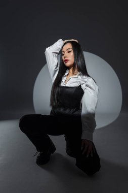 Sinirli moda kıyafeti giymiş modern bir kadın stüdyoda bacak bacak üstüne atmış oturuyor. Spot ışığı güçlü özelliklerini ve kendine güvenen duruşunu vurguluyor. Asyalı güzel kadın.