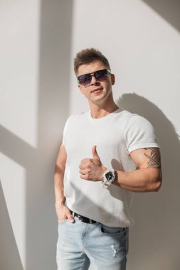 Yakışıklı, başarılı, güneş gözlüklü, beyaz tişörtlü sağlıklı bir adam. Güneş ışığındaki beyaz duvar gibi.