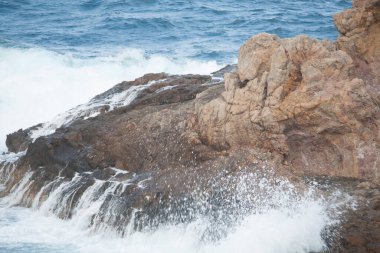 Dalgalar denizin kıyısındaki kayalara çarpıyor.