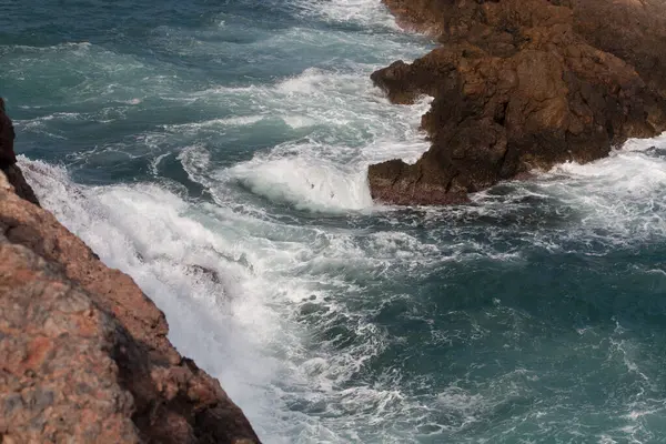 Deniz dalgaları kayalık kıyılara çarpıyor.