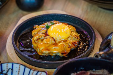 Tsukimi Tavuğu Teppanyaki Kıymalı Tavuk Orijinal Tarifle Baharatlı, sıcak bir tabakta kızartılana kadar Teriyaki sosu ve yumurta sarısı ile kaplanana kadar.