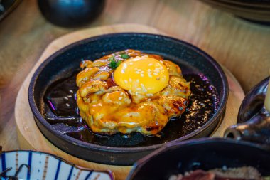 Tsukimi Tavuğu Teppanyaki Kıymalı Tavuk Orijinal Tarifle Baharatlı, sıcak bir tabakta kızartılana kadar Teriyaki sosu ve yumurta sarısı ile kaplanana kadar.