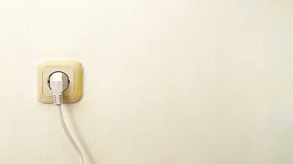 stock image Black power cord cable plugged into wall outlet on white plaster wall with copy space, socket, vintage