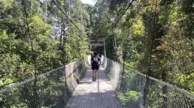 Turist, uzun köprü, yürüyüş ya da yürüyüş yolu ile en uzun asma köprüde yürüyen erkek, yeşil ormandaki ağaç tepelerinde arka planda dağ ile birlikte asma köprü