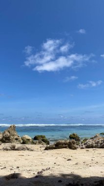 Kayalıklı bir sahil ve arkasında birkaç bulut olan mavi bir gökyüzü.