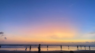 Güzel turuncu gün batımı plajda insanlar ve pembe, mor ve mavi bir gökyüzü.