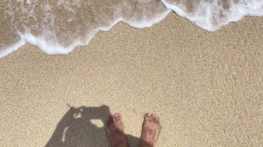 Bir insan kumsalda ayakta duruyor ayakları havada ve gölgesi kumların üzerinde..
