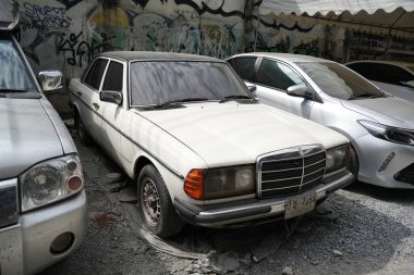 Bangkok, Tayland - 27 Kasım 2024: Eski ve terk edilmiş Mercedes Benz arabası, kırsal ve harap olmuş lüks sedan barı yan yola park edilmiş.