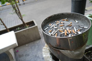 Bir sürü yanmış sigara izmariti ve sigara içme alanındaki kül tablasında biraz kül.