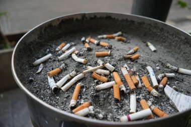 Bir sürü yanmış sigara izmariti ve sigara içme alanındaki kül tablasında biraz kül.