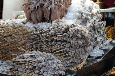 Izgara kalamar tezgahı sokak yiyecek tedarikçisinde, yanında taze mürekkep balığı yığını var.