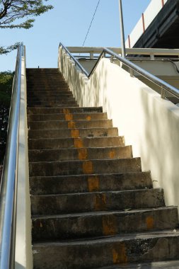 Mavi gökyüzünün arka planına uzanan yamaçtan yukarı çıkan tırabzanlı beton merdivenler. Şehrin demiryolu köprüsünün yanındaki aşınmış merdivenler.