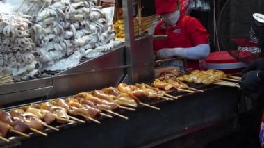 Bangkok, Tayland. 21 Kasım 2024 - sokak pazarı tedarikçisi yiyecek standında ızgara kalamar şişleri, taze deniz ürünleri mürekkep balıkları hazırlıyor.