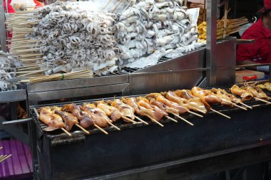 Taze kalamar ızgara sokak tezgahı satıcısı, Tayland 'da bir markette sopayla ızgara kalamar.