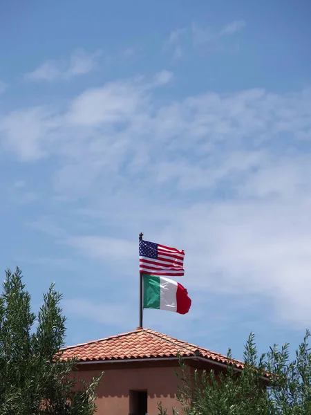 US American flag and Italian flag waving above a tile roof