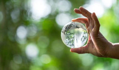 Kristal küre, belli bir nesne olarak kullanılır. Arka planda ağaçlar olan doğa parkı. Yeşil arka planda sürdürülebilir ve etik sektörde çevre, sosyal ve yönetim için eller.