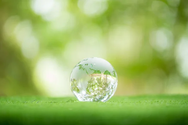 Close up of crystal globe resting on grass in a forest - environment concept. environmental, social, and governance in sustainable and ethical business on green background.