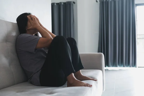 Schizophrenia with lonely and sad in mental health depression concept. Depressed woman sitting against on the sofa at home with dark room feeling miserable. Women are depressed, fearful and unhappy.