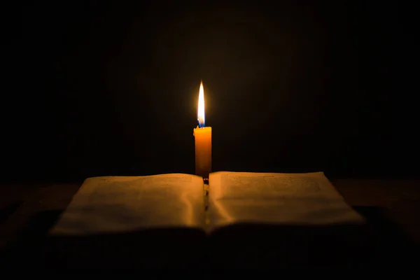 用圣经上的点燃的蜡烛和十字架或十字架钉在教堂古老的木制背景上 烛光和打开的旧式木桌书 家庭中的基督教学习和阅读 基督宗教的概念 — 图库照片