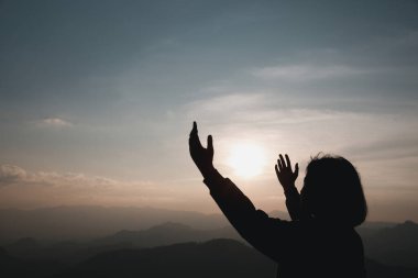 Faith christianity of christian worship concept. Spiritual prayer hands over sun shine with blurred beautiful sunset background. Woman praying to god with hopeful blessing against sunset.