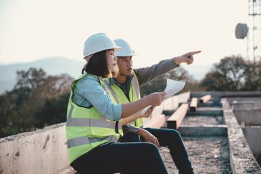 Two specialists inspect commercial, Industrial building construction site. Real estate project with civil engineer, designing commercial buildings on paper. Skyscraper concrete formwork frames.