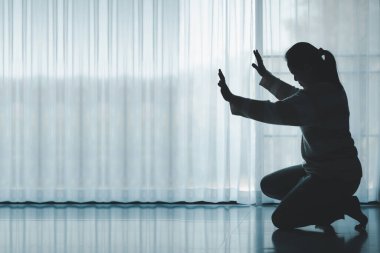 silhouette of woman kneeling and praying in modern church at sunset time. Female catholic prayer worship to God wish a better life in home at dawn with believe faith. concept of worshipers kneeling.