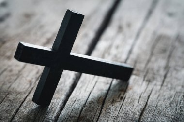 A wooden Christian cross crucifix on a grunge board background. Wooden Christian cross on grey table against blurred lights, space for text.