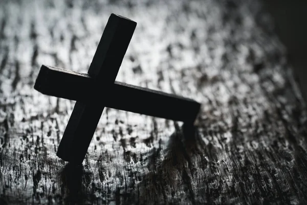 A wooden Christian cross crucifix on a grunge board background. Wooden Christian cross on grey table against blurred lights, space for text.