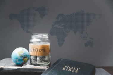 Para dolu kavanozlar ve kutsal İncil 'le görev için, Hıristiyanlık misyonu fikri. İncil ve kitap ahşap masa üzerinde, Hıristiyan arka planı büyük komisyon veya Toprak Günü konsepti için.