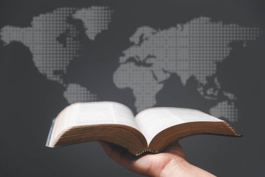 Hand holding Holy Bible and world map in blur background. World mission christian idea. Copy space for text. Christian background for great commission or earth day concept. clipart