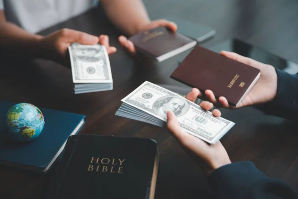 Concept of Christian ministry. Small groups pray together for Christian mission. Mission to spread gospel and religion of Christianity around world. Hands holding dollar and passport on wooden table.