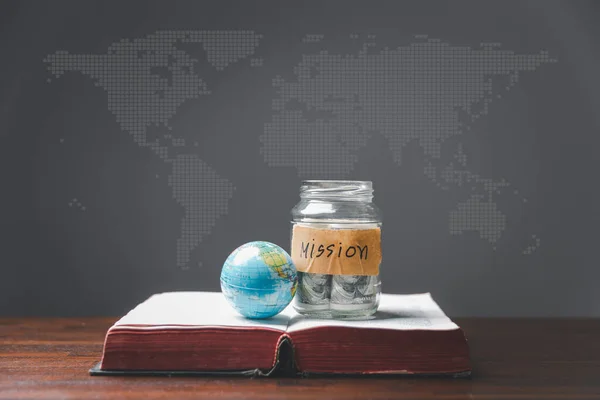 Savings jars full of money and globe with Holy Bible for mission, Mission christian idea. bible and book on wooden table, Christian background for great commission or earth day concept.