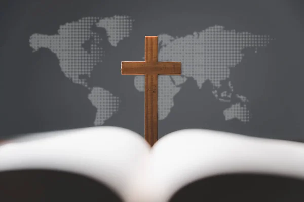Cross with open Holy Bible on table with world map blur background. mission evangelism and gospel on world. Copy space for text, Christian background for great commission or earth day concept.