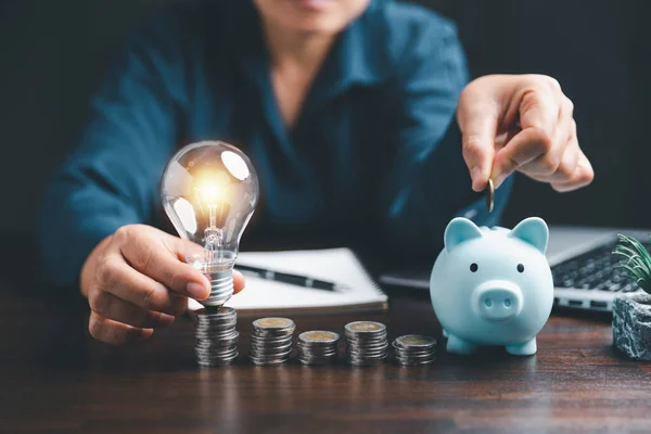 Businesswoman with lightbulb and piggy bank and using calculator to calculate and money stack. Save energy and money with accounting finance in office concept. Idea of energy saving planning in home.